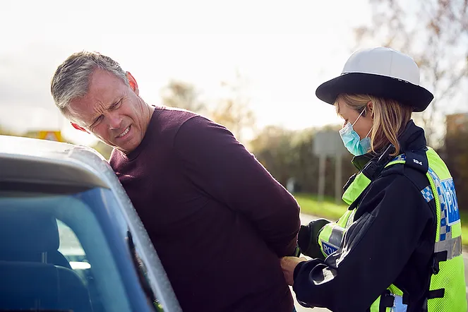 Man being arrested by female police officer by car