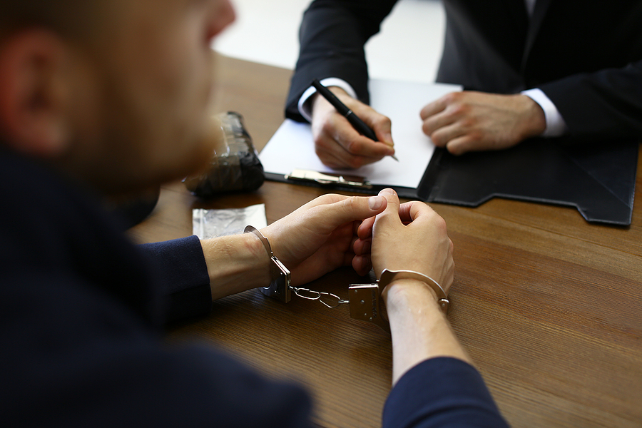 Police Officer Interrogating Criminal In Handcuffs At Desk